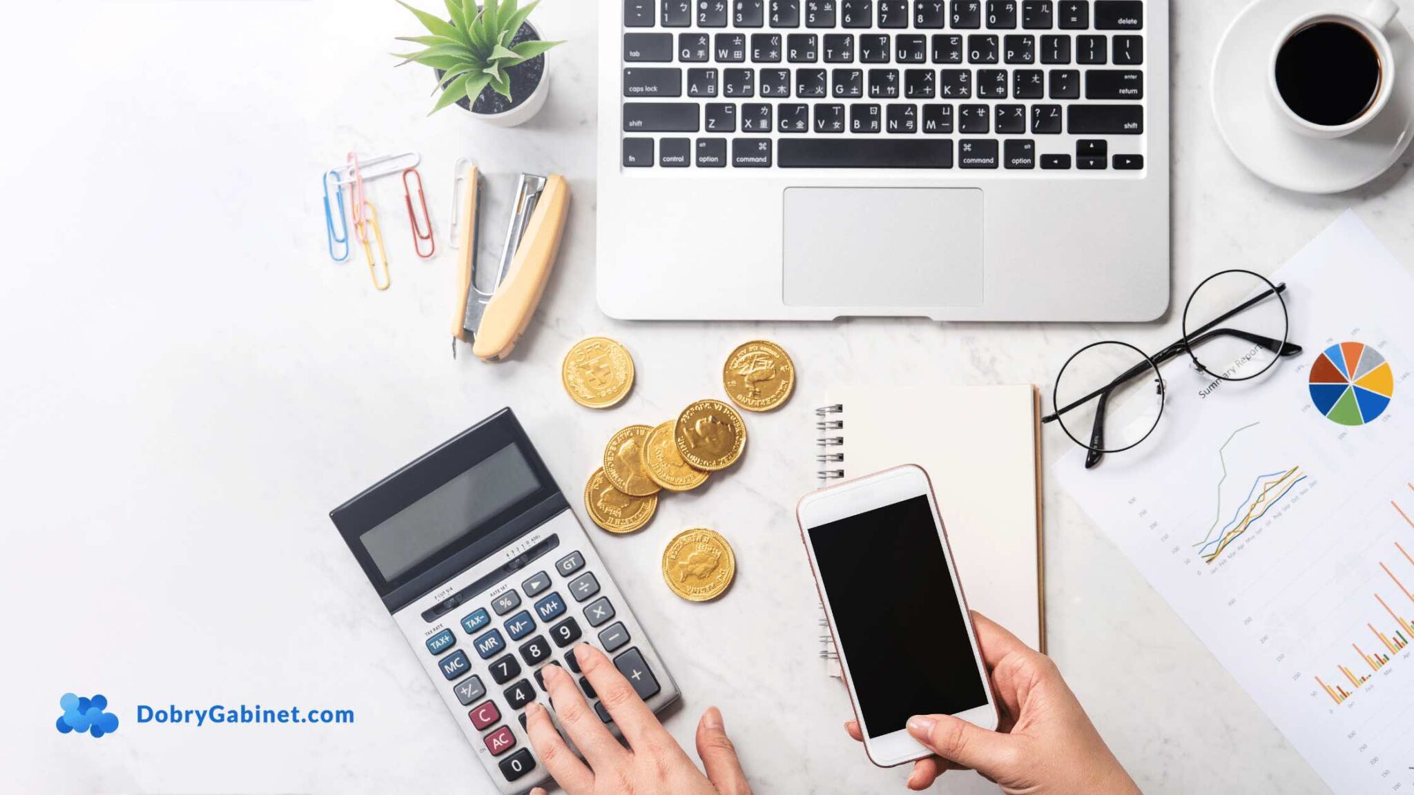 Top view of a workspace with a laptop, calculator, smartphone, coins, notepad, plant, and charts on a white desk.